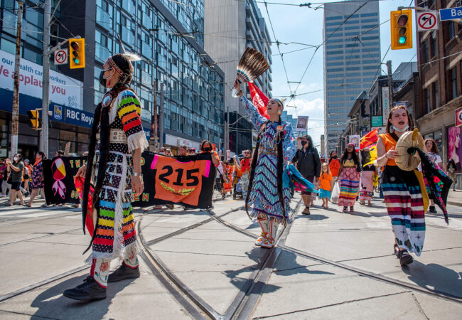 Indigenous people dressed in regalia walk in a march on the city streets in honour of the children whose unmarked graves were uncovered at Kamloops Indian Residential School.